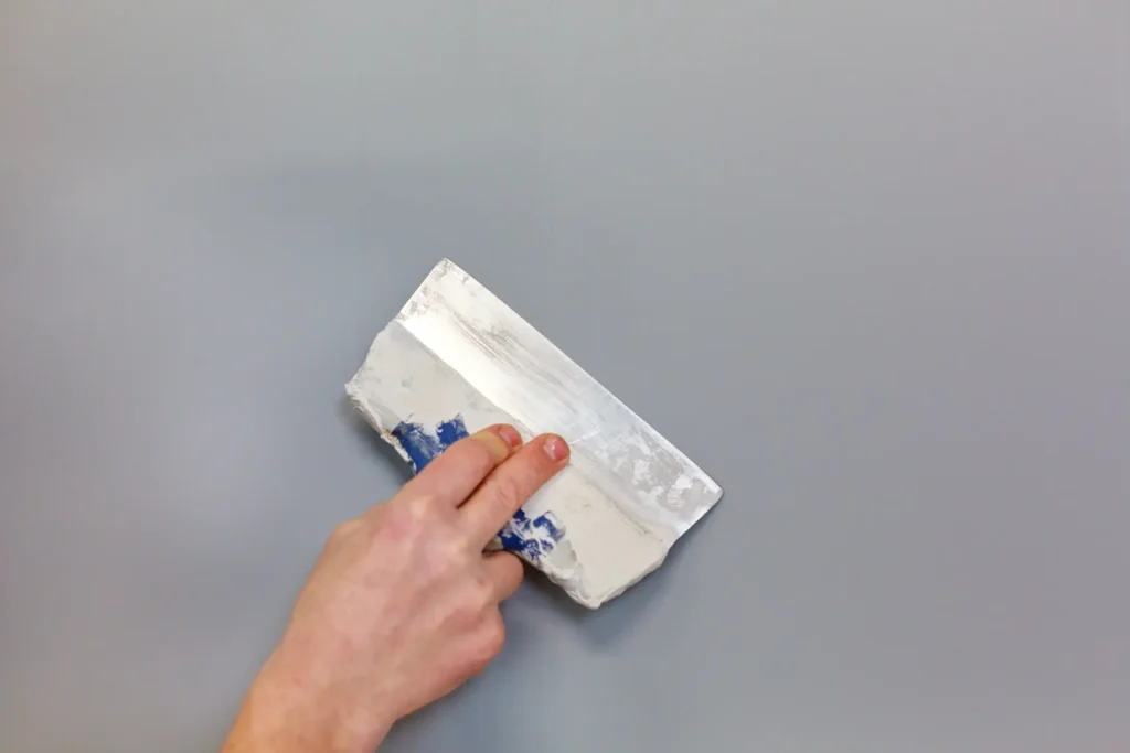 Hand håller spackelspade mot vägg