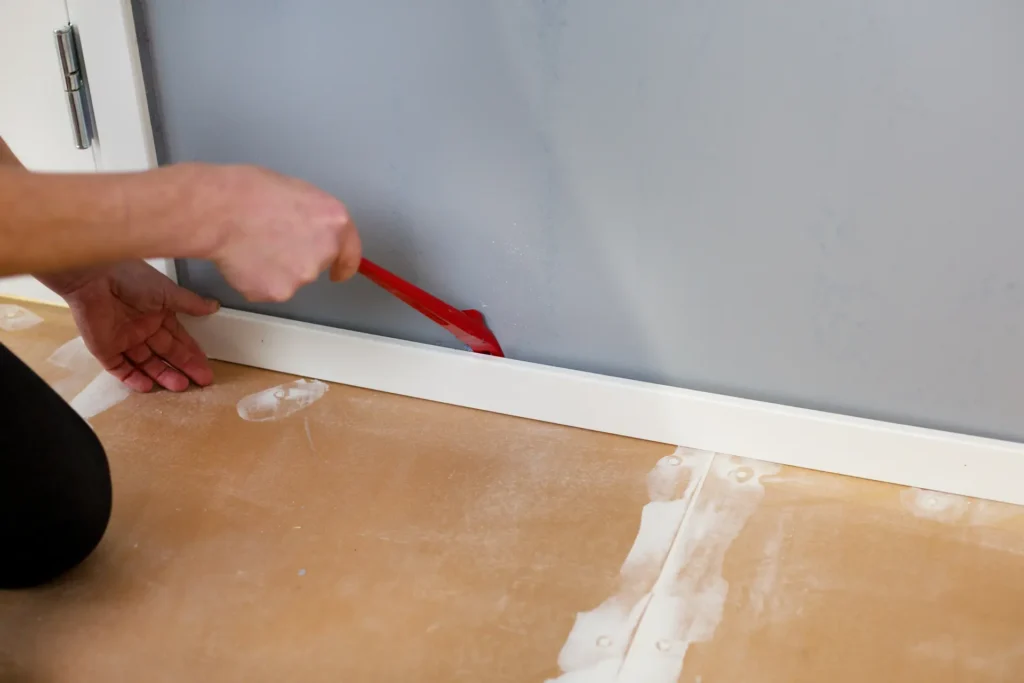 Person håller kofot mot golvlist vid montering av radontapet