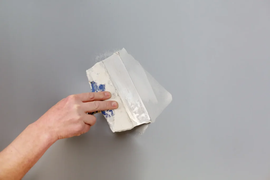 Hand håller spackelspade mot vägg