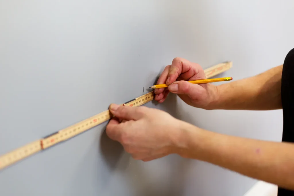 Person märker ut på vägg med penna och linjal